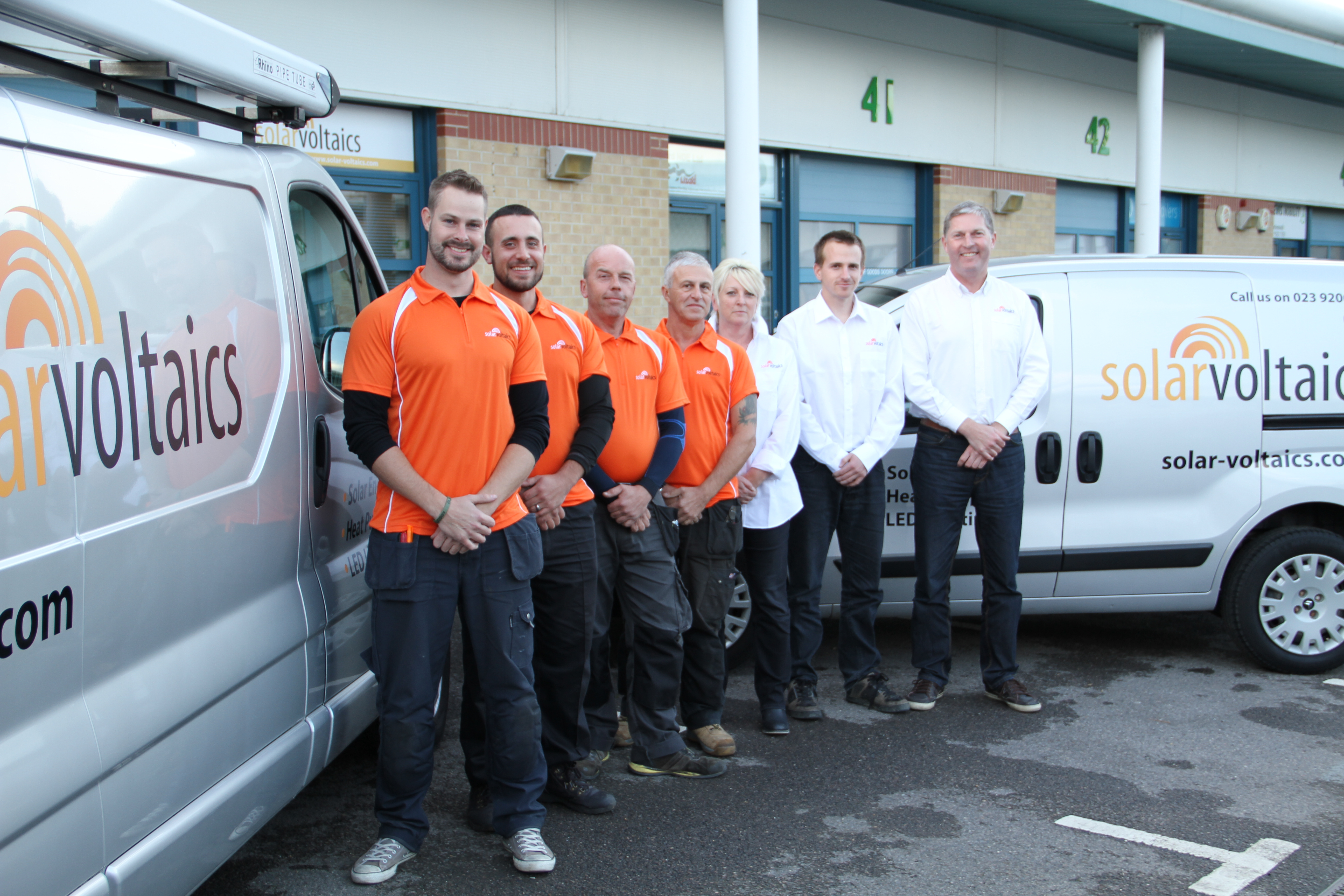 Solar Voltaics team photo - management and installation engineers in orange logo shirts - next to two of our vans
